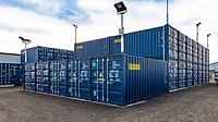 Self storage site with blue shipping containers stacked in rows, topped with light panels
