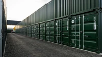 A long row of stacked green shipping containers at a self storage site, marked with numbers and lockboxes
