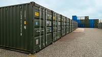 Row of green 20ft containers on a self storage site with stacked containers in the background