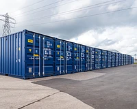 A long row of blue 20ft shipping containers on a self storage site